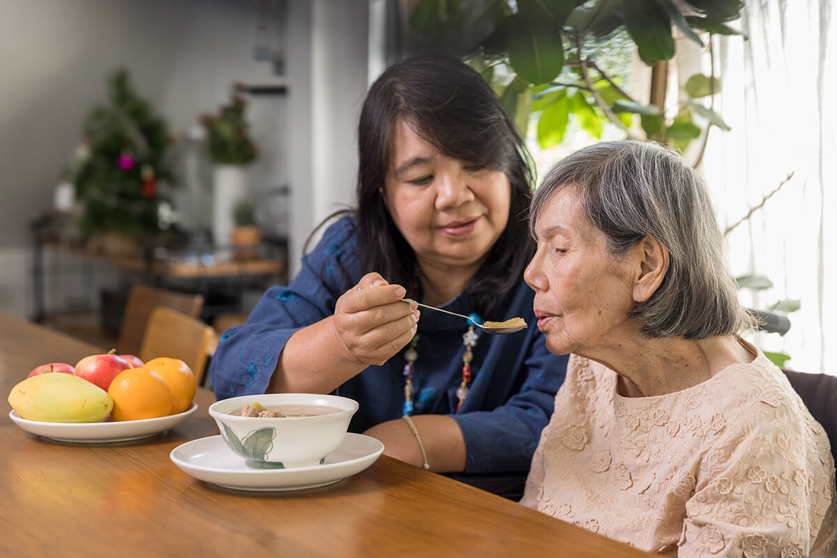 Caregiver feeding soup to senior woman at home